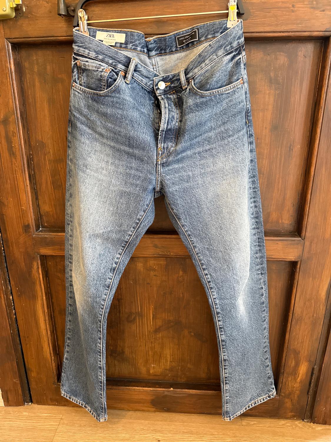 Worn blue jeans hanging on a wooden door. Visible labels on the waistband.