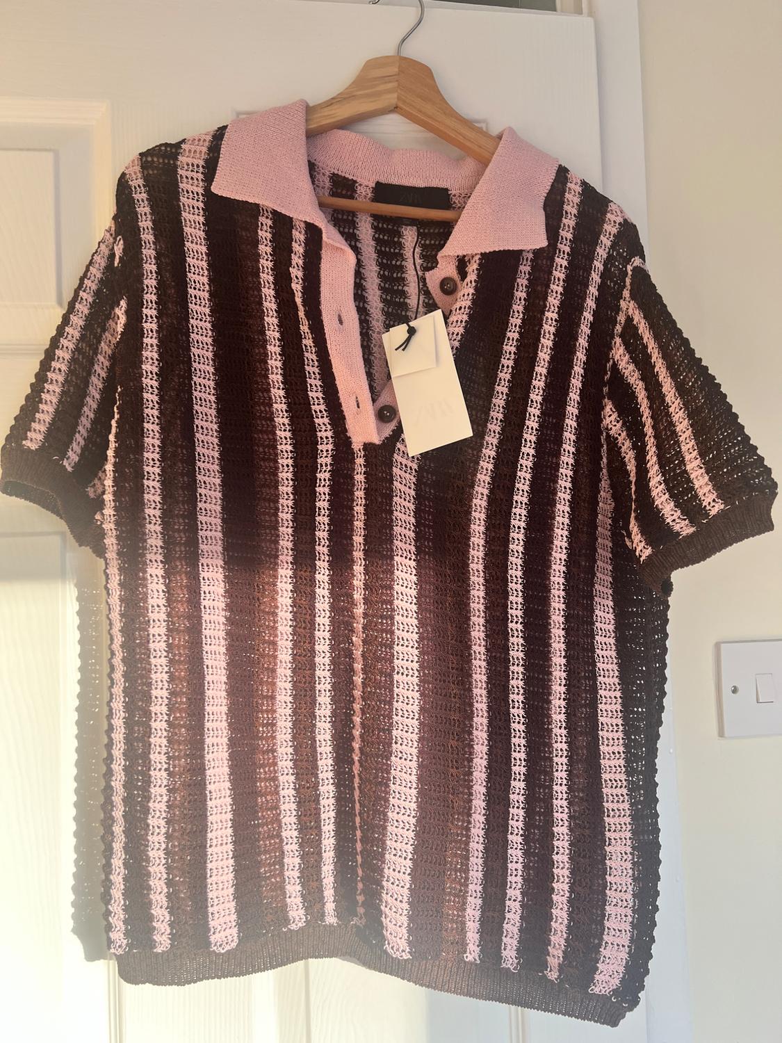 Knitted shirt hanging on a wooden hanger, with brown and pink vertical stripes, and a pink collar. White tag hanging.