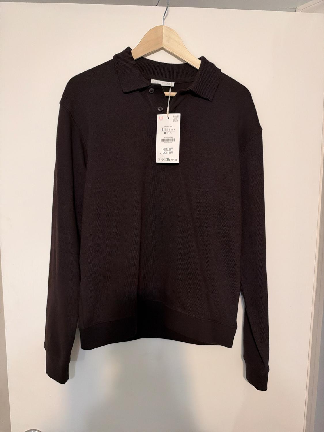 Dark brown long-sleeve polo shirt with a button-down collar and tag,
hanging on a wooden hanger over a white door.