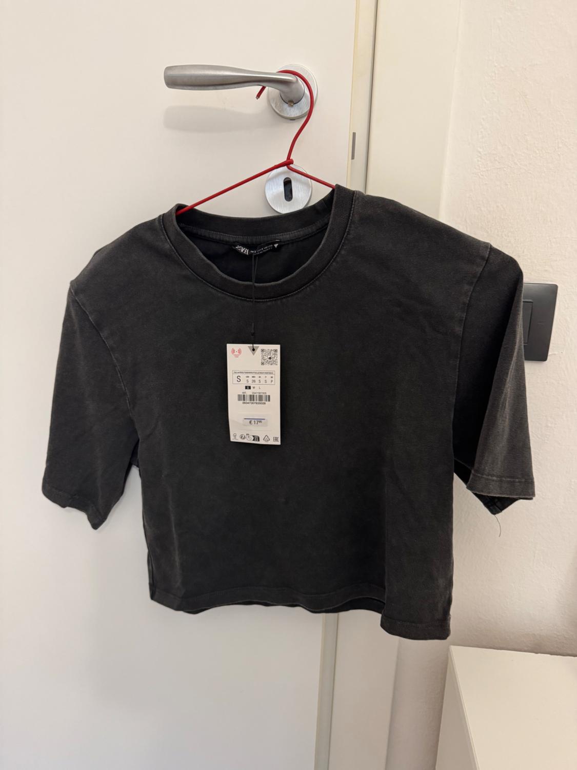 Black short-sleeved t-shirt hanging on a red hanger on a white door. Visible label with barcode and price.