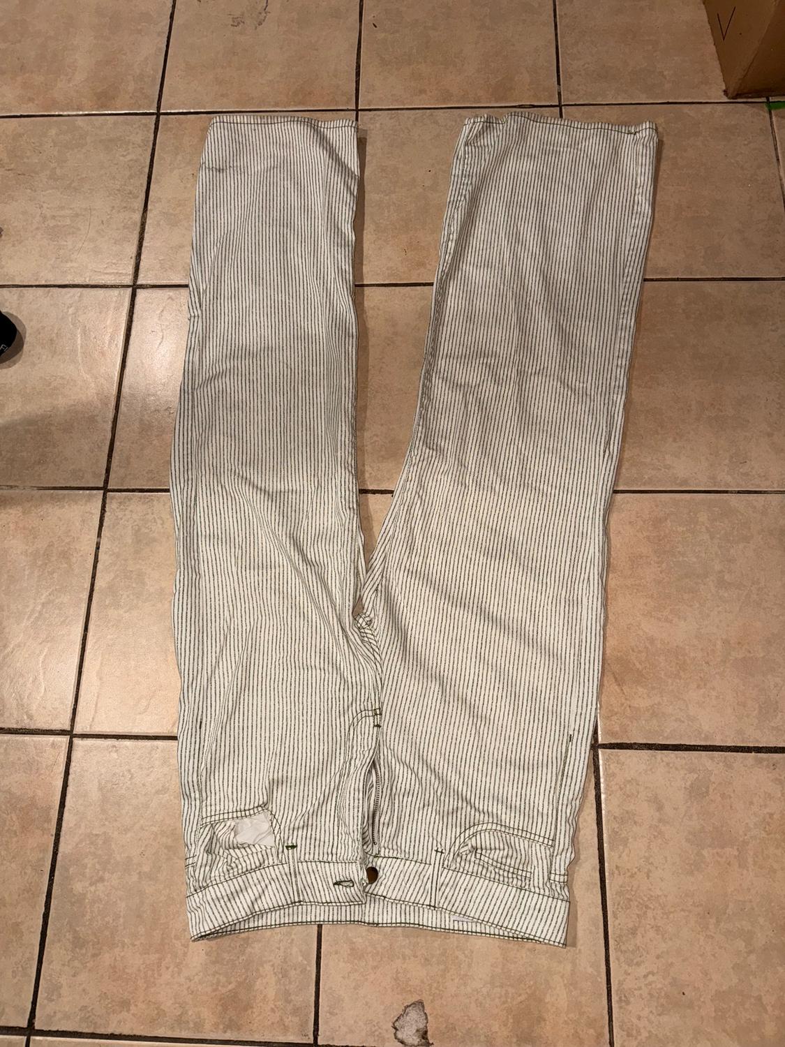White and gray striped pants spread out on a brown tiled floor. Bottom part of a garment visible.