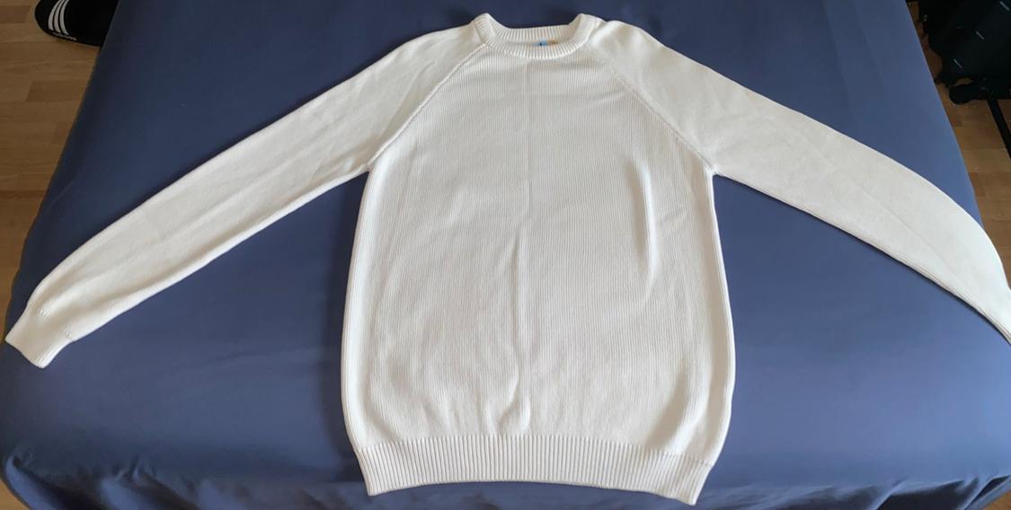 White knitted sweater with long sleeves and a crew neck, laid out on a blue sheet.