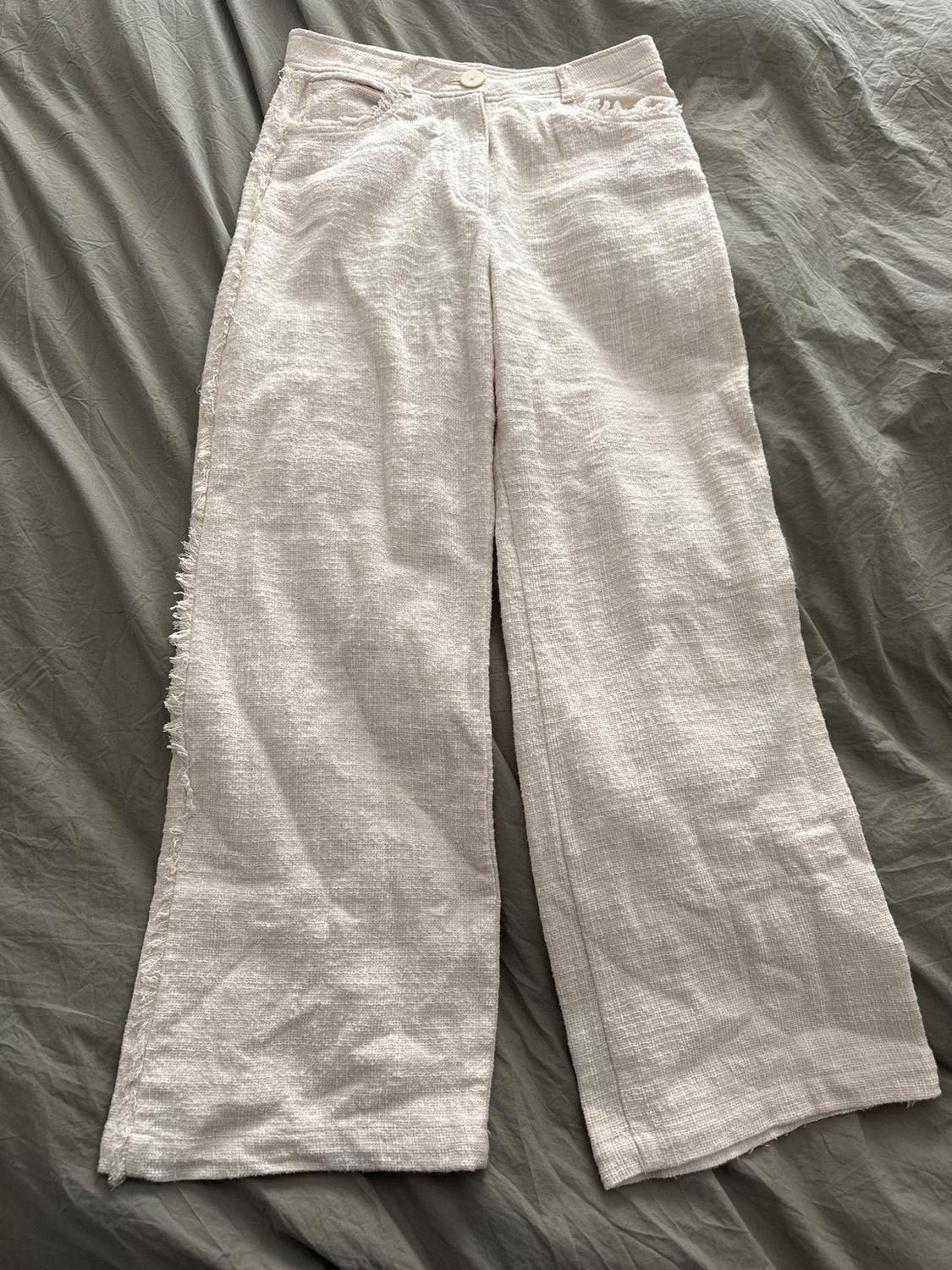 White textured fabric pants with buttons, placed on a wrinkled gray surface.