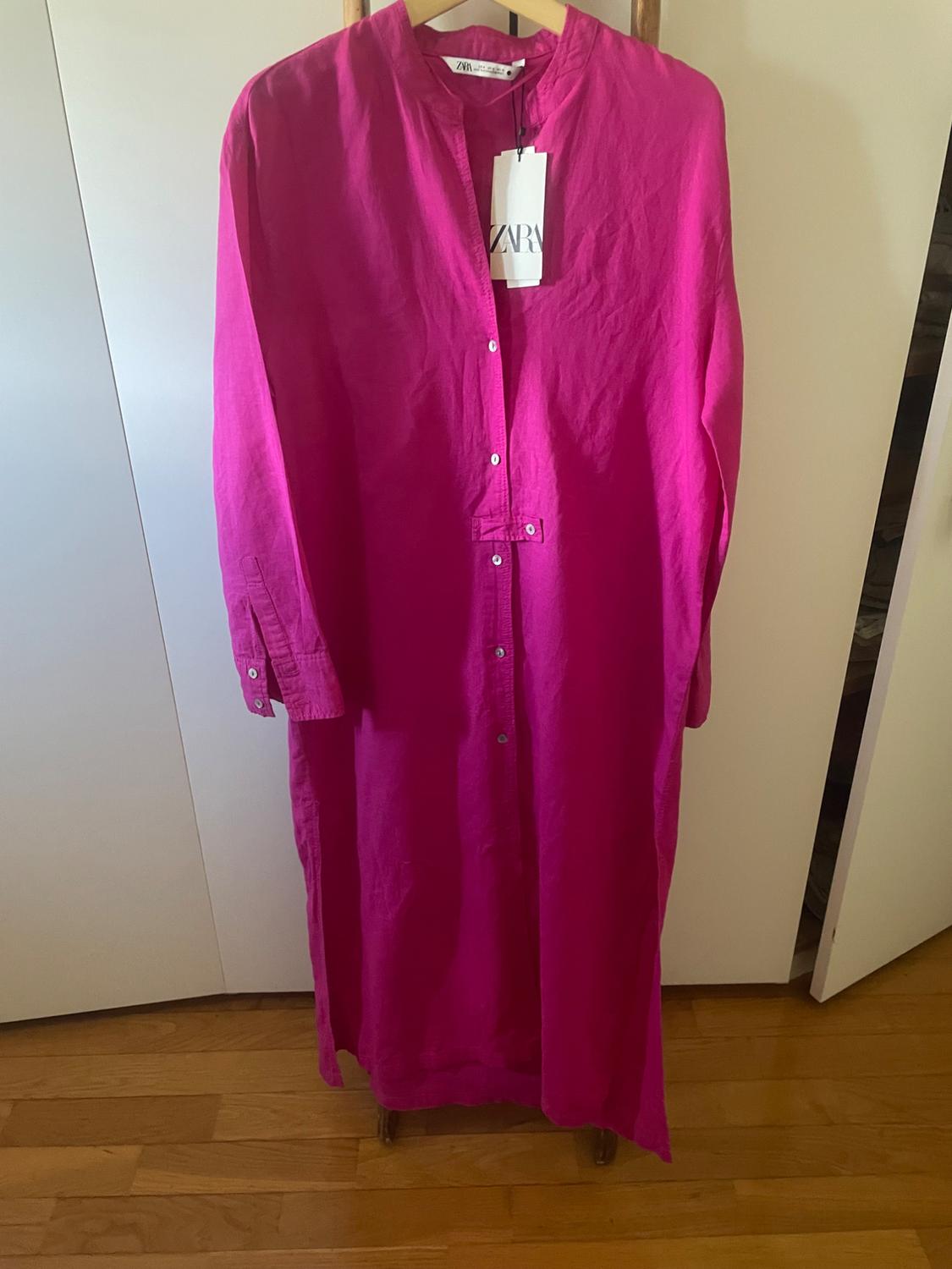 Fuchsia maxi dress hanging on a wooden coat hanger, with a visible Zara tag, against a white wardrobe background and wooden floor.