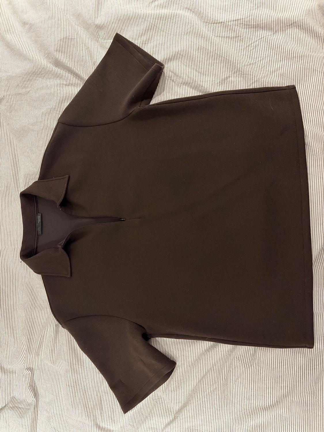 Brown short-sleeved polo shirt with a zip, on a fine white and grey striped fabric.