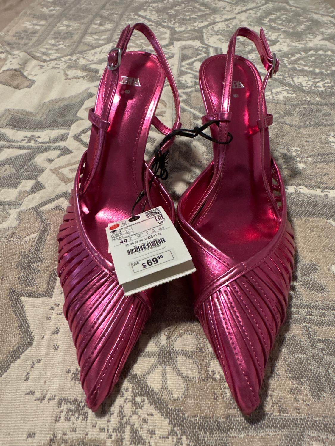 Metallic pink high heels with a $69.90 price tag on a textured neutral-toned surface.