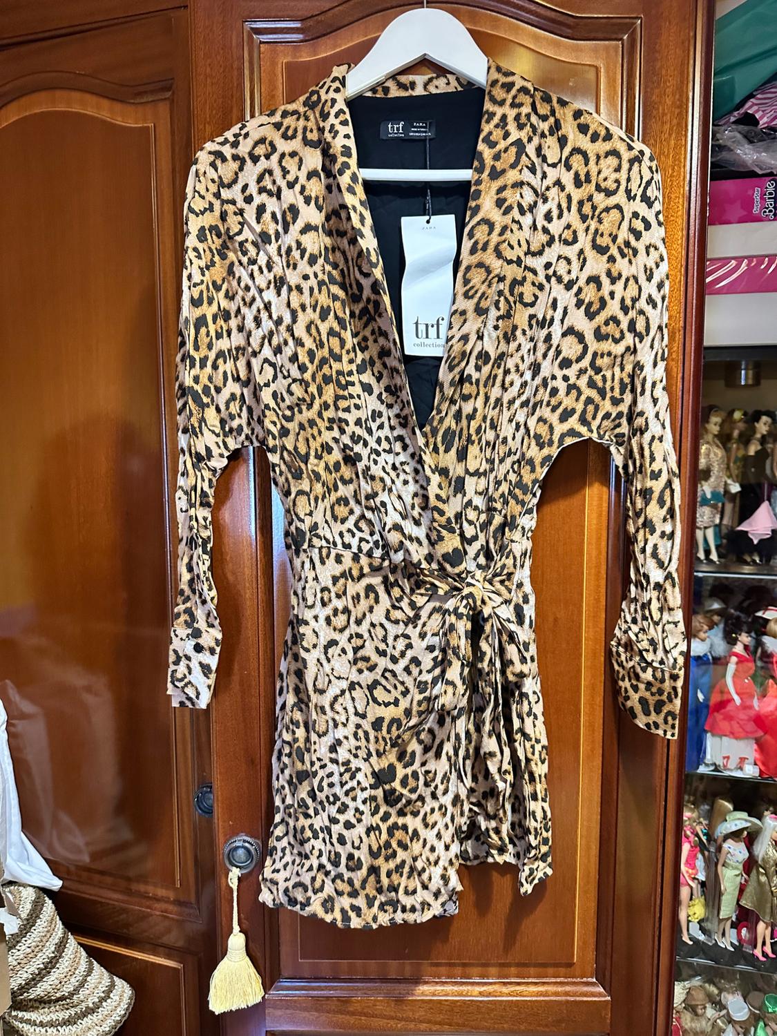 Leopard print wrap dress hanging in a wooden wardrobe. TRF Collection ZARA label. Relaxed setting with a dolls' display cabinet in the background.