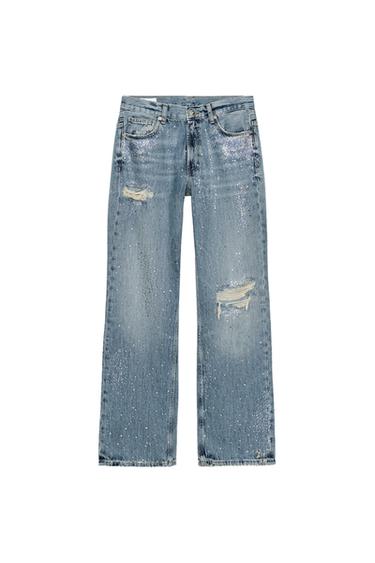 Front view of low-rise, wide-leg blue jeans, ripped at the knees, with rhinestones and five pockets. Zip and button fastening.