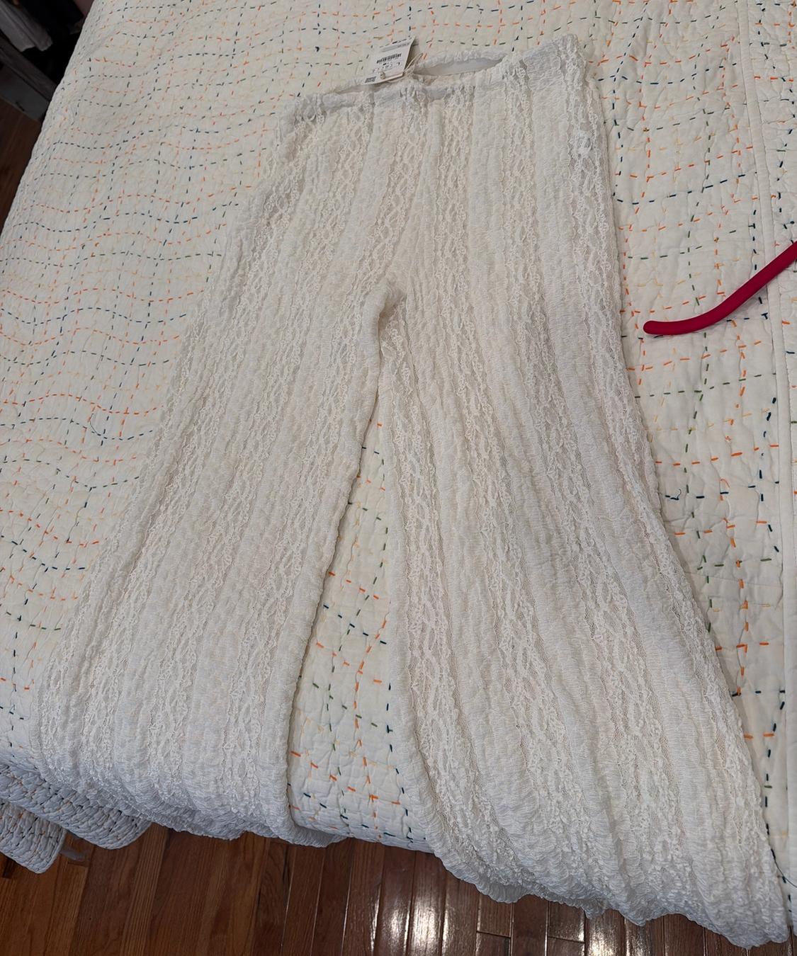 Long, wide-leg white pants with lace texture, laid out on a bed with a white quilt featuring colorful stitching.