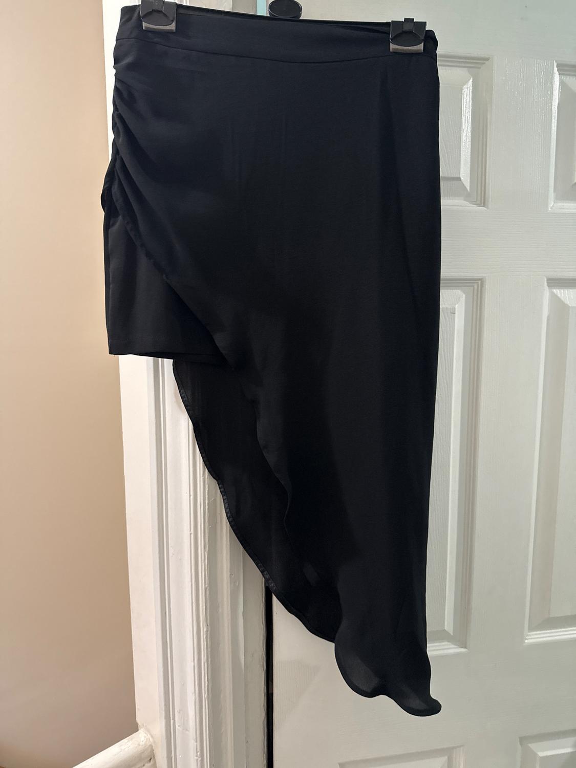 Asymmetrical black skirt hanging on a white door, with a draped design on the left side.