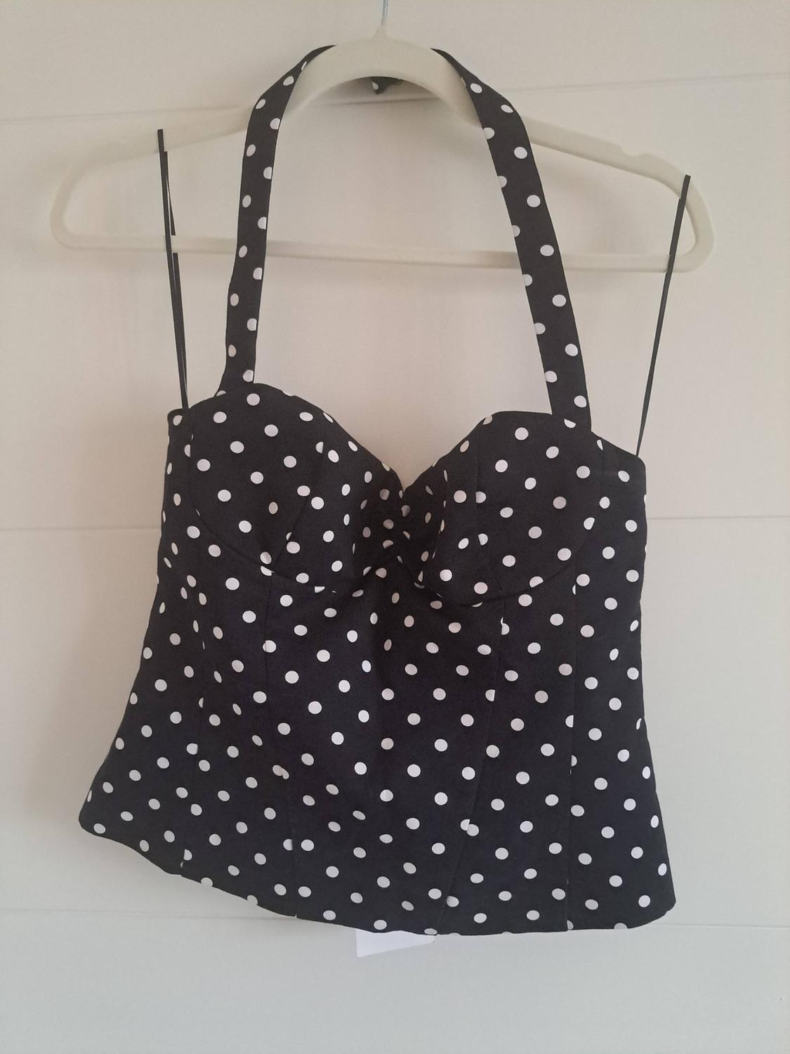 Black polka-dot top with a sweetheart neckline and halter neck, hanging on a coat hanger against a white background.