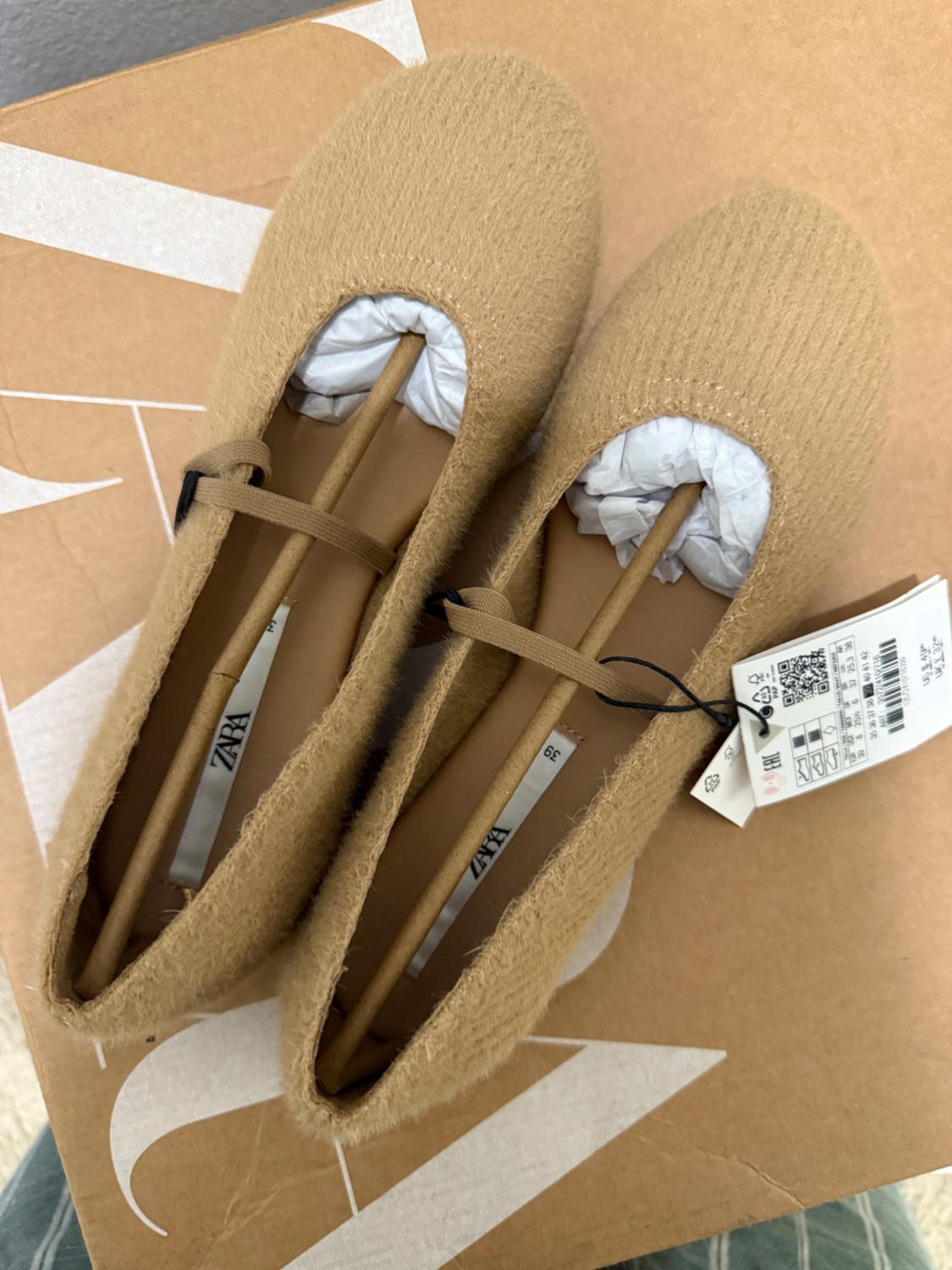 Beige soft fabric shoes with tag, on brown box with white design. Visible inner label with text "ZARA".