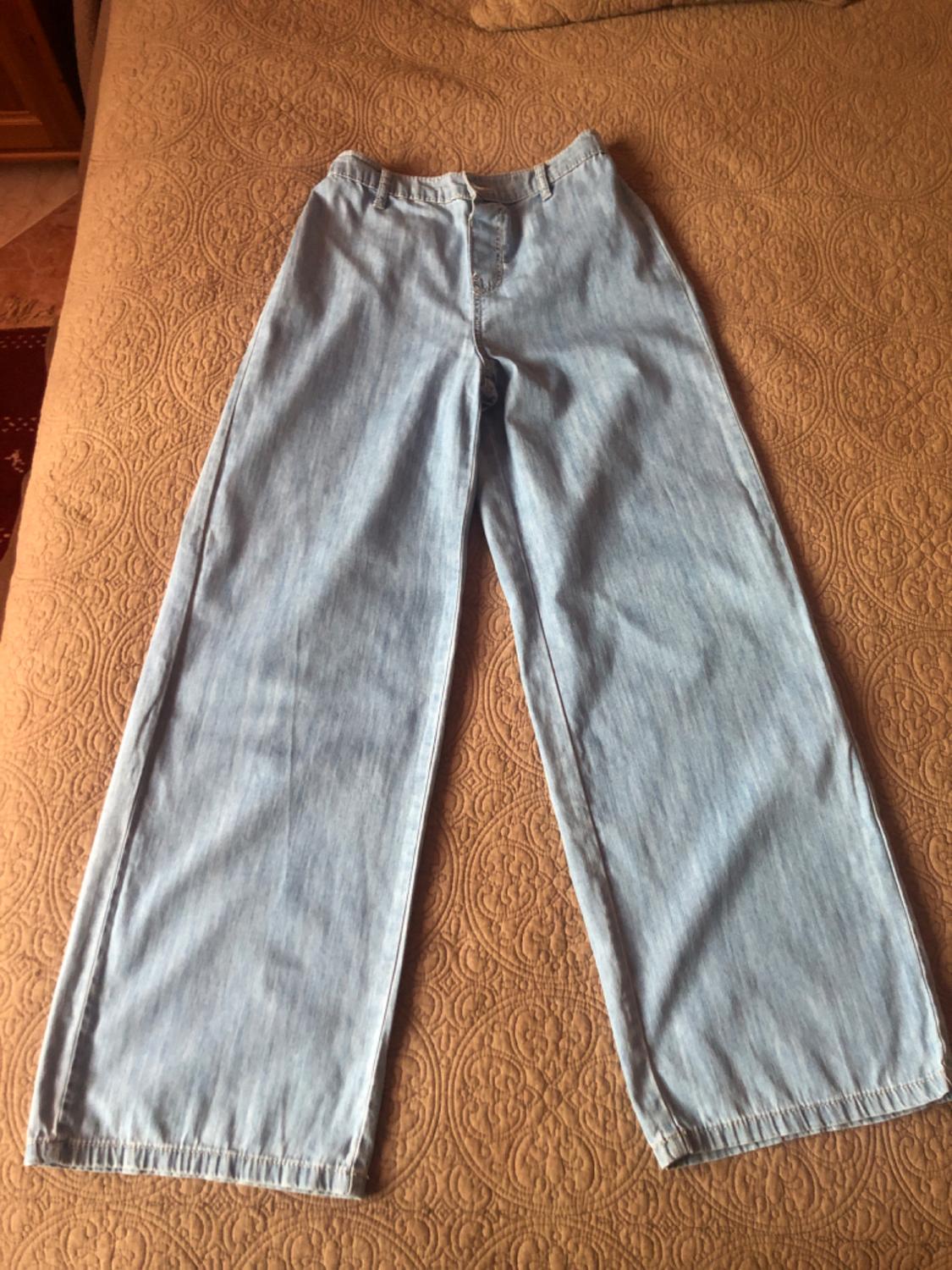 Light blue wide-leg jeans, placed on a bedspread with a circular pattern design.