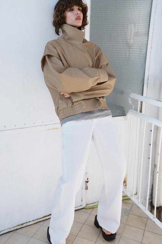 Béžová bunda s rolákem a široké bílé kalhoty.