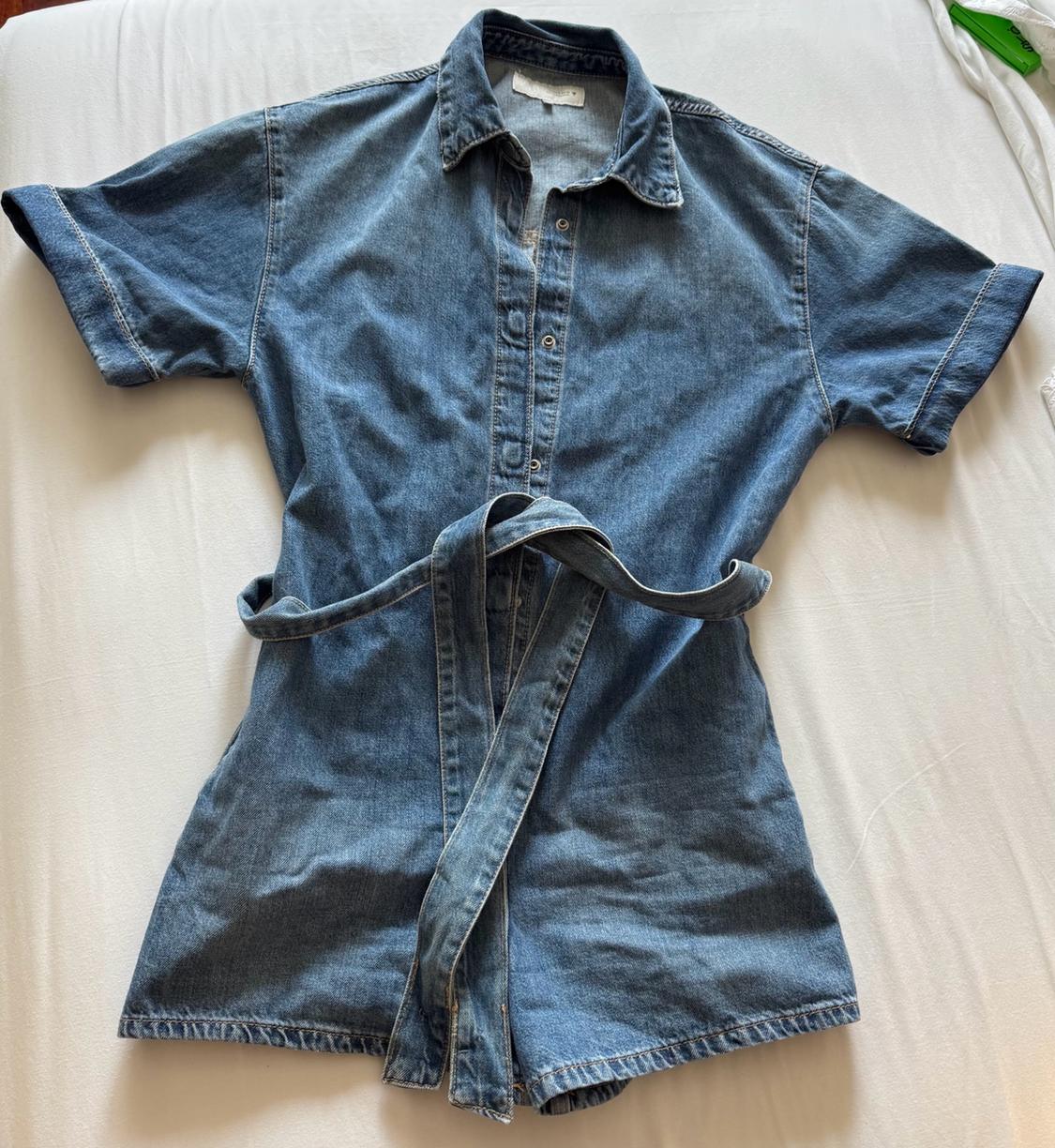 Blue short-sleeved denim playsuit with buttons and a tie belt, laid out on a white sheet.