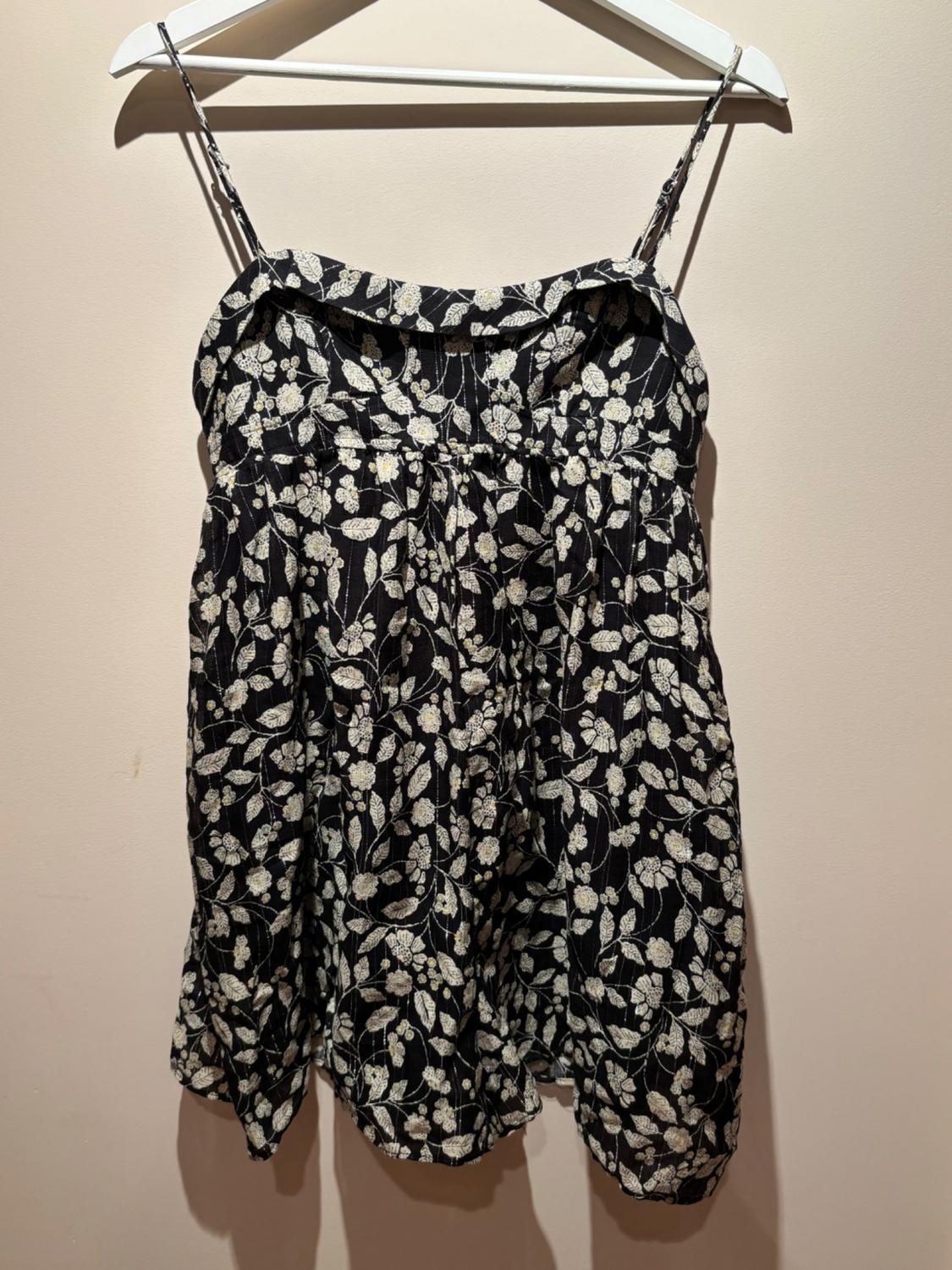 Black sundress with white floral print, hanging on a white hanger against a beige background.