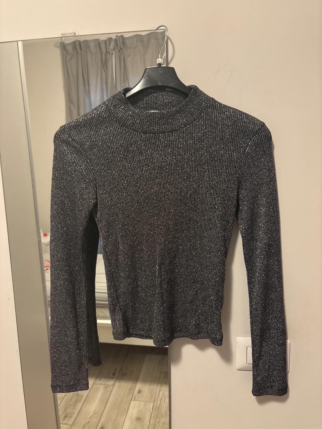 Shiny grey ribbed long-sleeved high-neck top hanging on a hanger against a white wall next to a mirror.