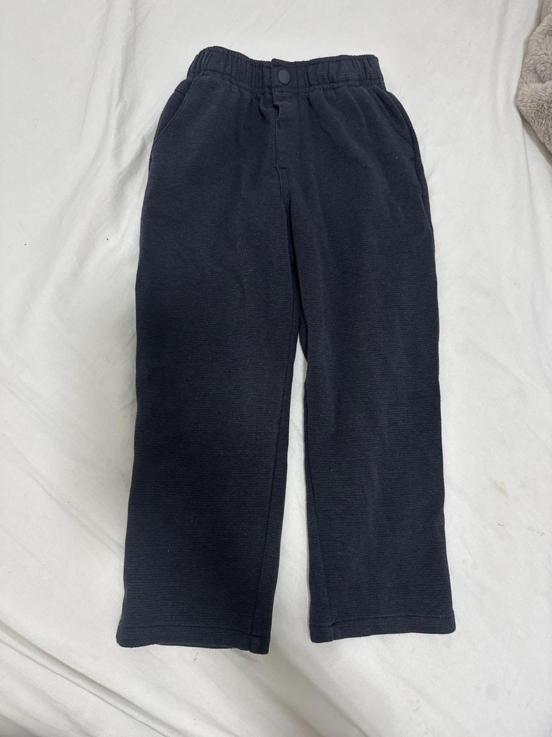 Dark casual-style pants with an elastic waistband, laid out on a white fabric surface.
