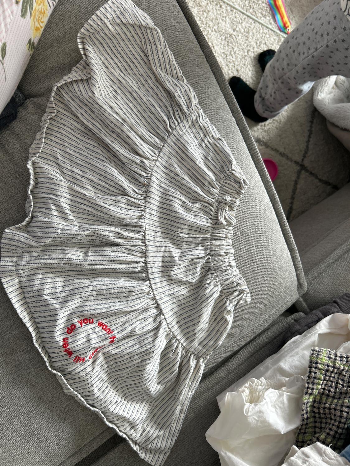 Grey striped mini skirt on a grey sofa. Red text on the skirt: "when do you want it". Background with a rug and clothes.