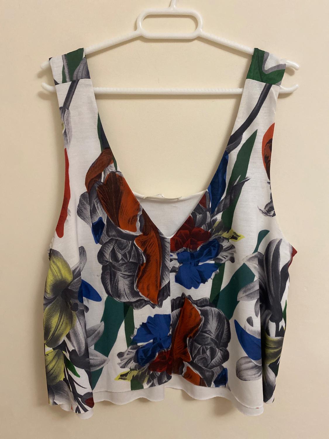 Front view of a sleeveless blouse with a brightly coloured floral print on a white background.