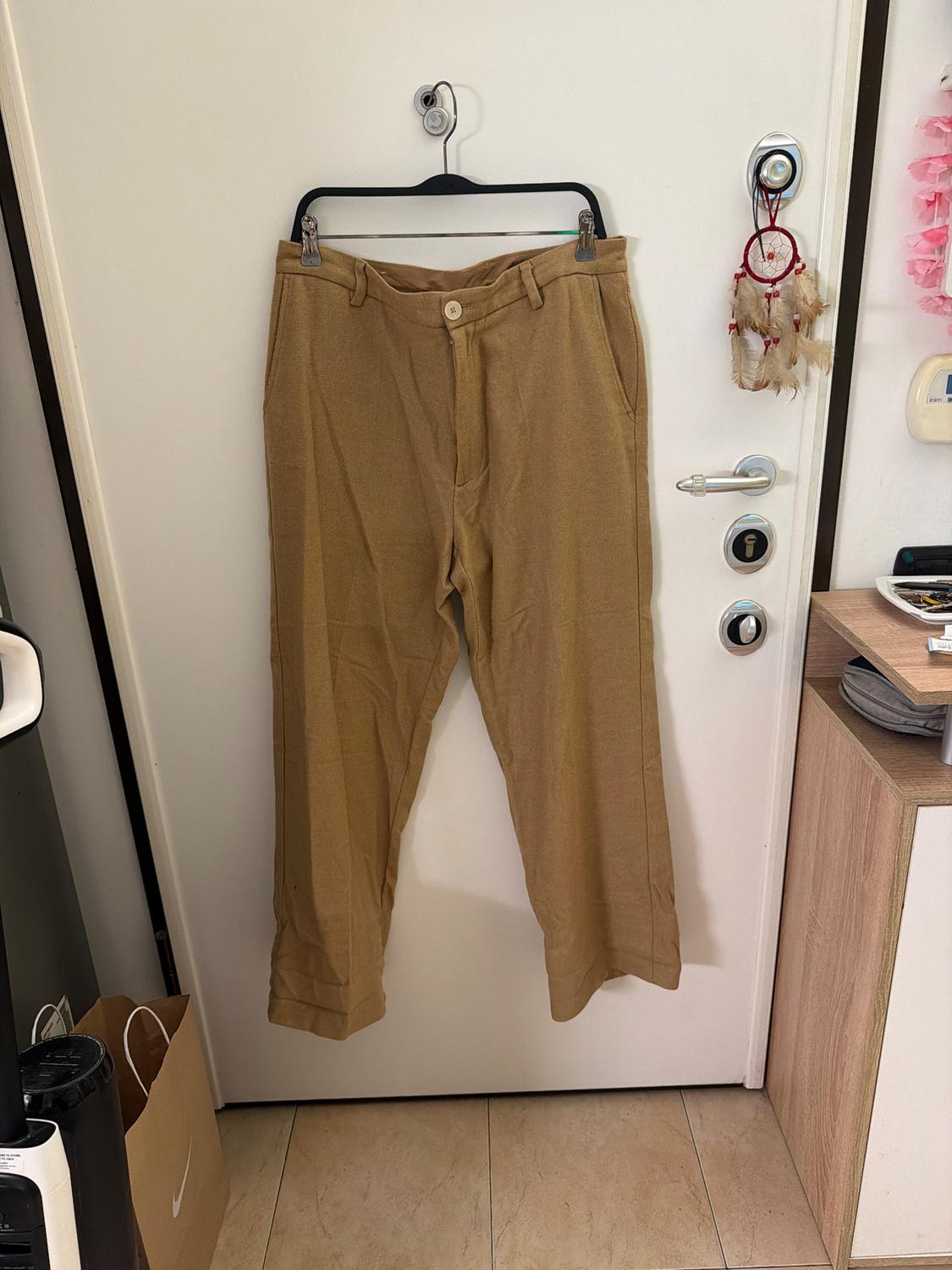Beige trousers hanging on a black hanger over a white door. To the right, a dreamcatcher with red feathers and beads.
