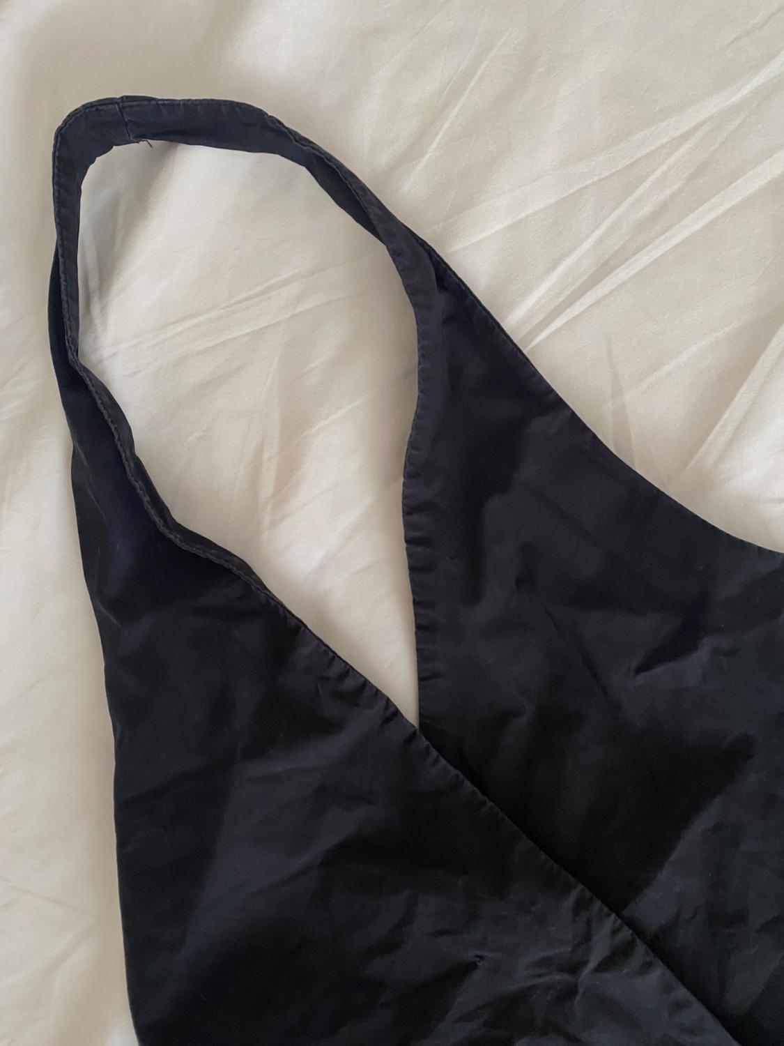 Close-up of a black garment with a deep V-neck and wide straps, over a wrinkled white fabric in a relaxed style.