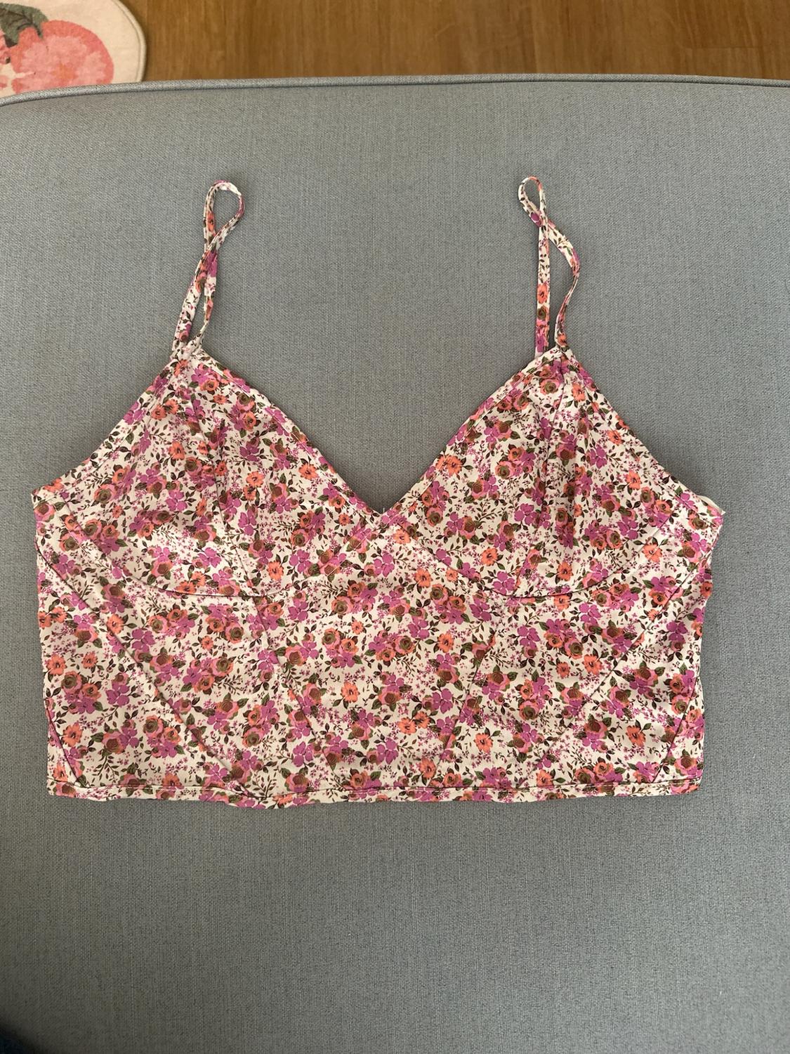 Pink floral print camisole crop top with a V-neck, laid on a grey fabric surface.
