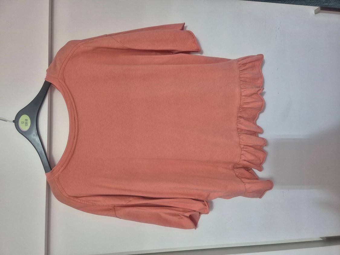 Pink long-sleeved t-shirt with frilled hem hanging on a black hanger against a white background. Text: 12 EUR 40.