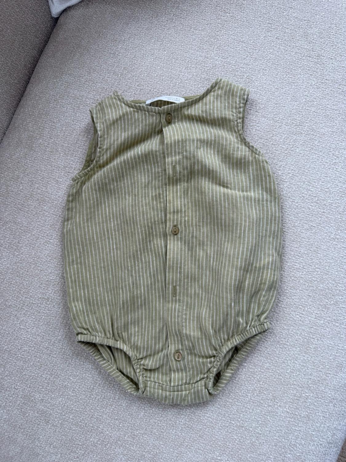 Olive-green sleeveless baby romper with white vertical stripes, front button closure, and elastic leg openings.