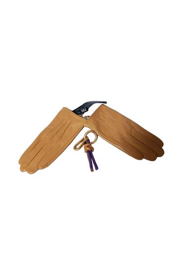 Brown gloves with decorative stitching, accompanied by a gold keyring with purple and beige details. White background.