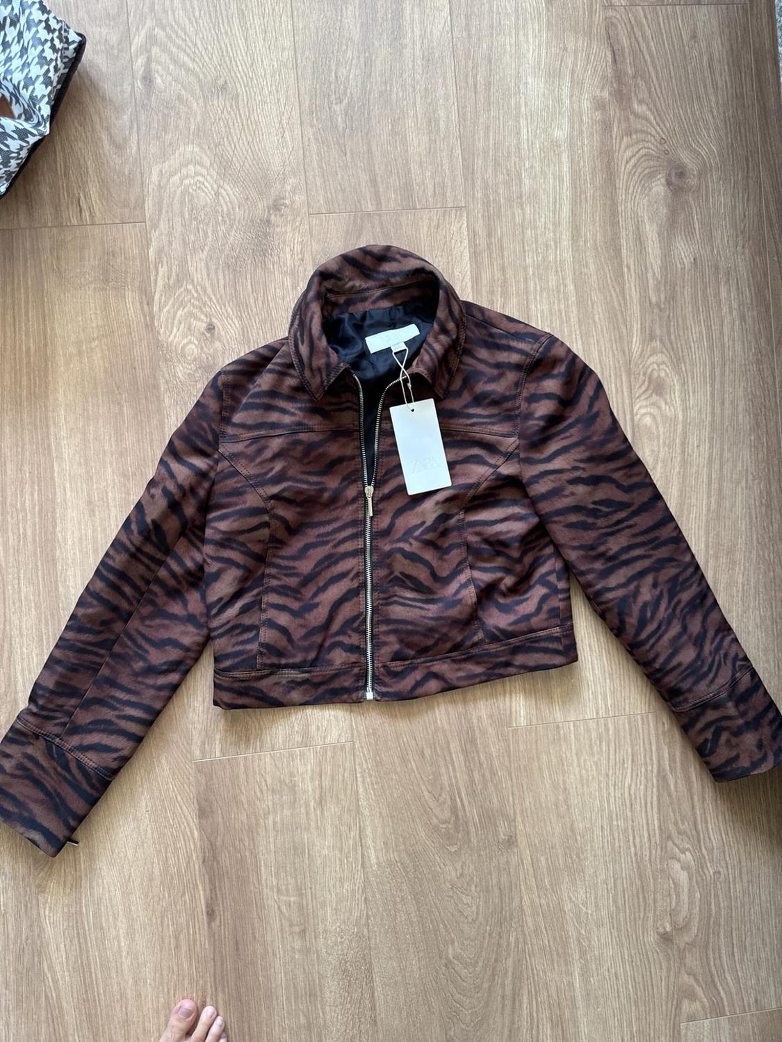 Brown and black animal print jacket, with a front zip and white label, laid out on a light wood floor.