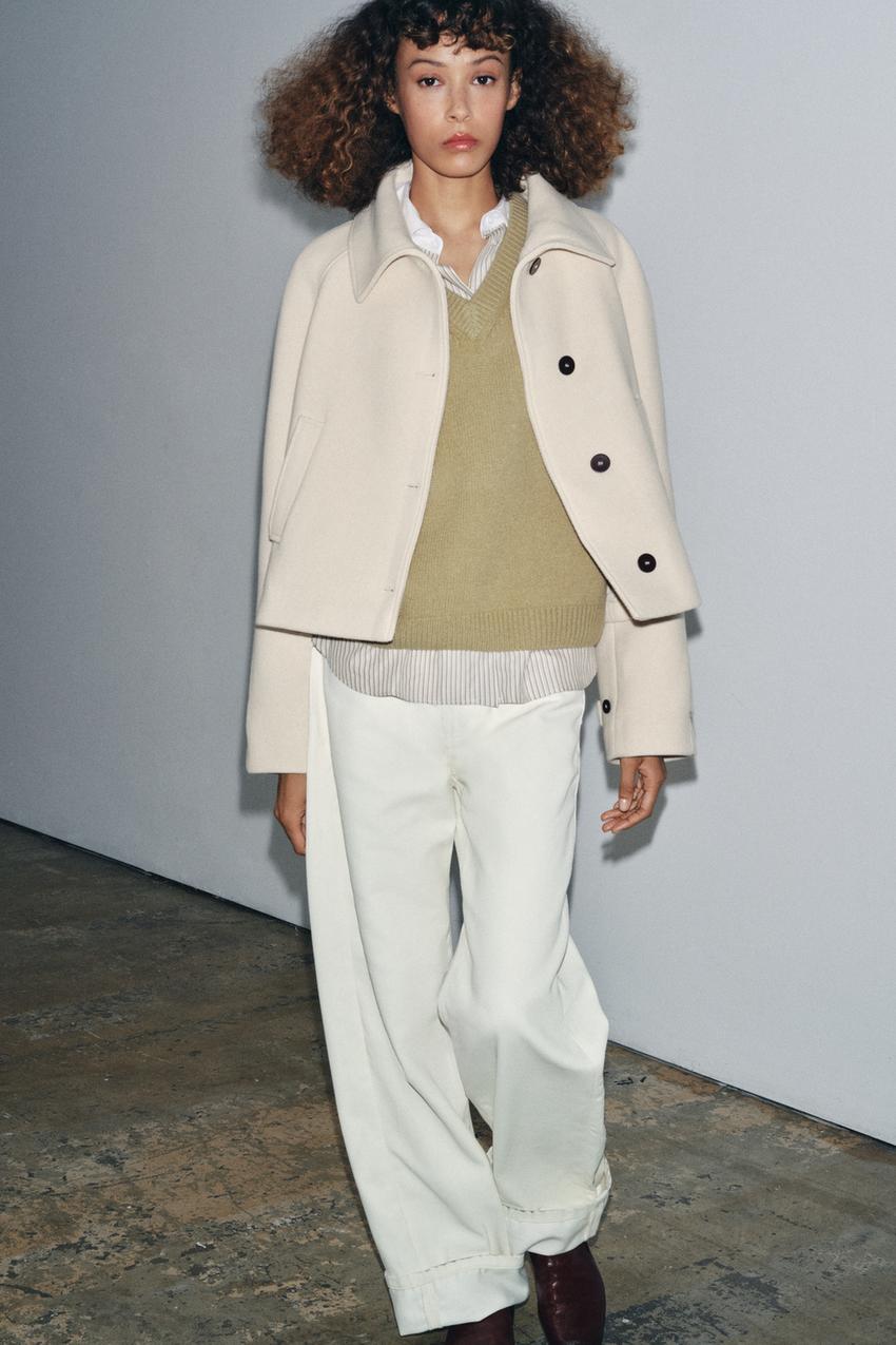 Raw short trench coat set with shirt collar, green sweater, striped shirt, and wide white pants.