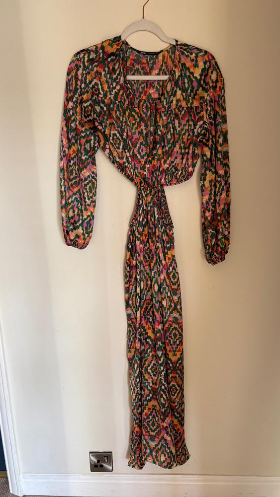 Long dress with a multicoloured geometric print in shades of green, pink, and orange, hanging on a white hanger.