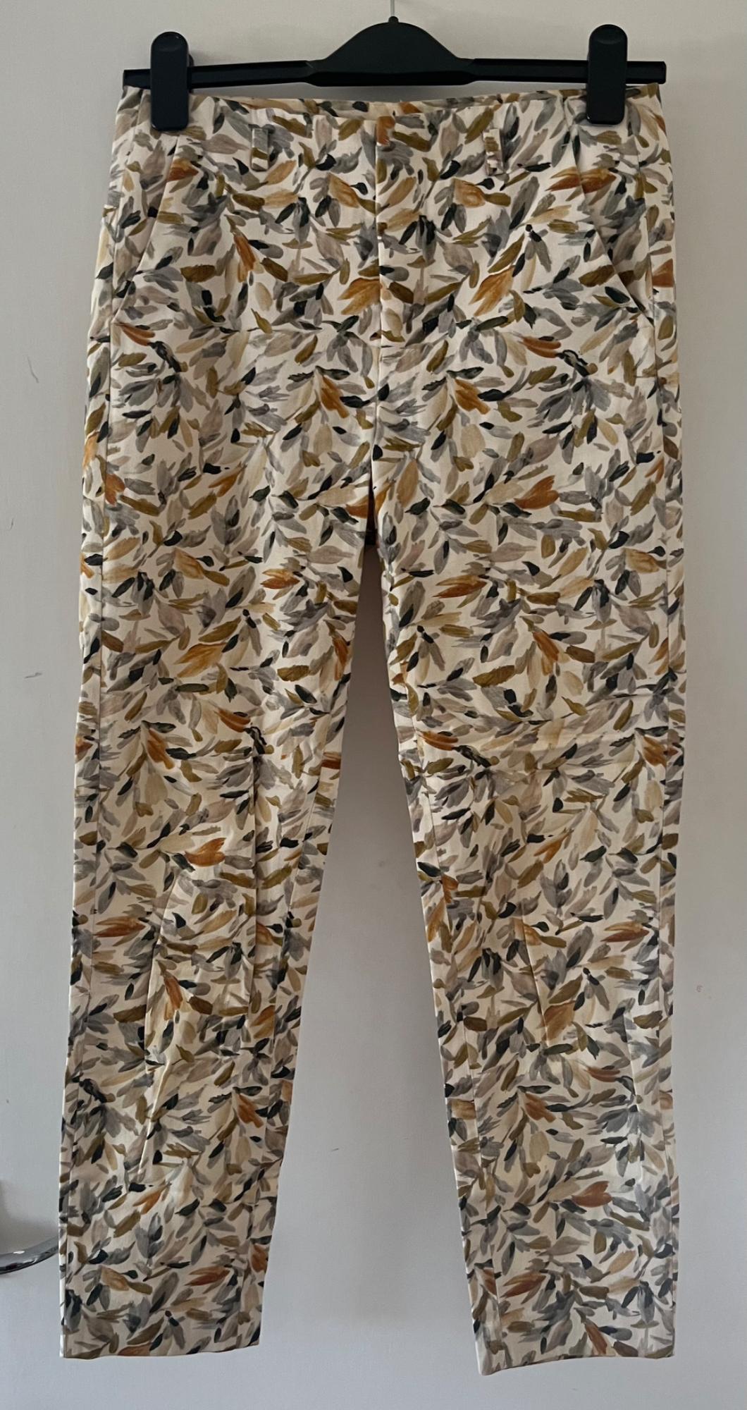 Trousers with a leaf print in shades of brown and grey, hanging on a black hanger against a white background.