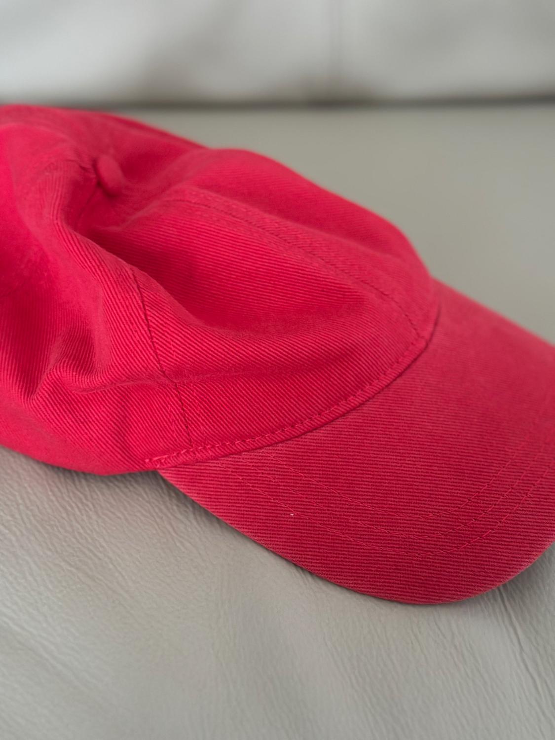 Red fabric cap on a light grey background, showing stitching details and material texture.