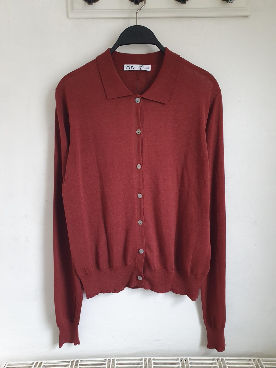 Red long-sleeved cardigan with buttons, hanging on a black hanger with a visible Zara tag, against a white background.