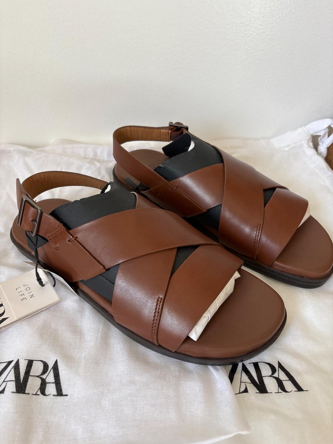 Brown strappy crossover sandals on a white bag with the "ZARA" logo. Visible tag with text "JOIN LIFE".