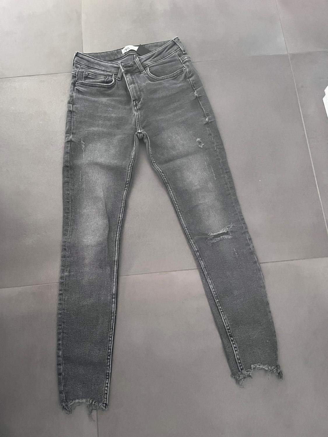 Washed-out grey jeans with ripped details on the legs, placed on a grey floor.