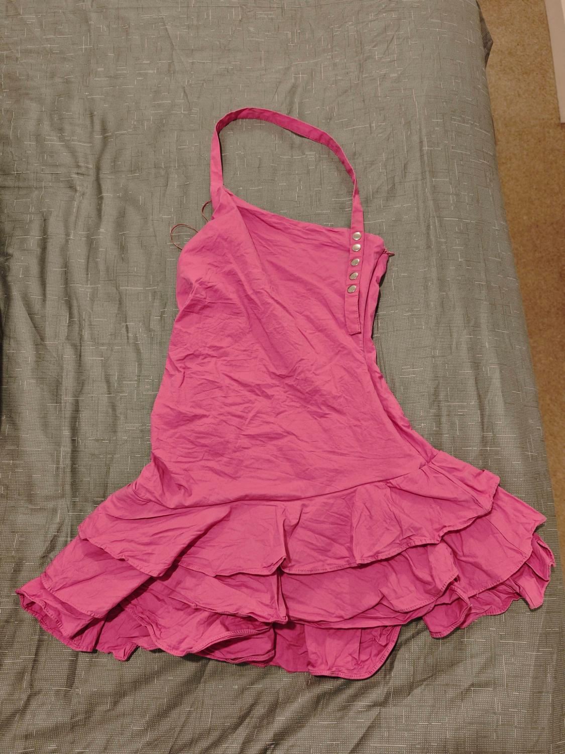 Pink short dress with a halter neck, buttons on one side and a ruffled skirt, spread over a textured grey bedspread.