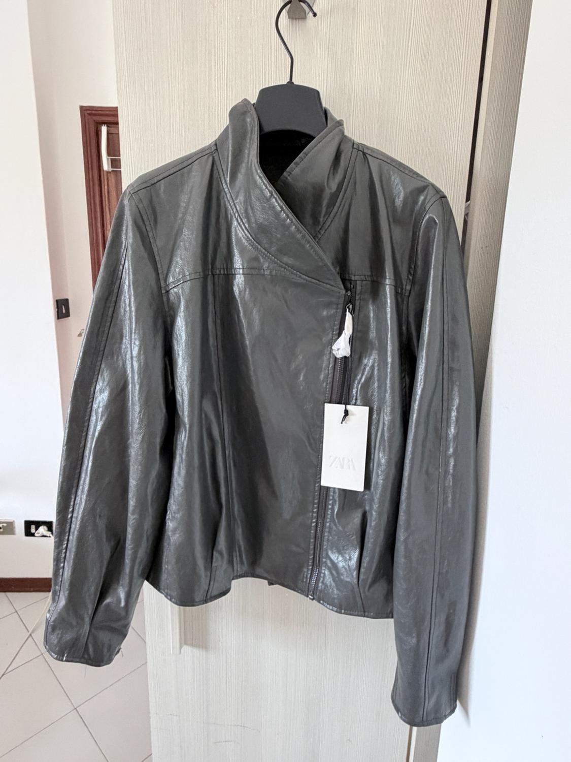 Dark grey zipped jacket hanging on a hanger over a door. It has a white label with the text ZARA.