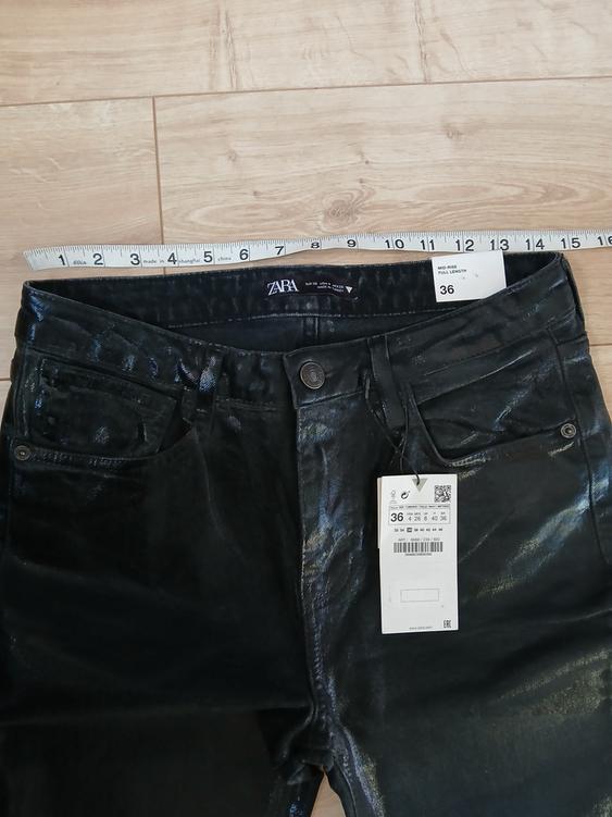 Shiny black Zara trousers on a wooden floor, with a size 36 label and tape measure showing measurements.