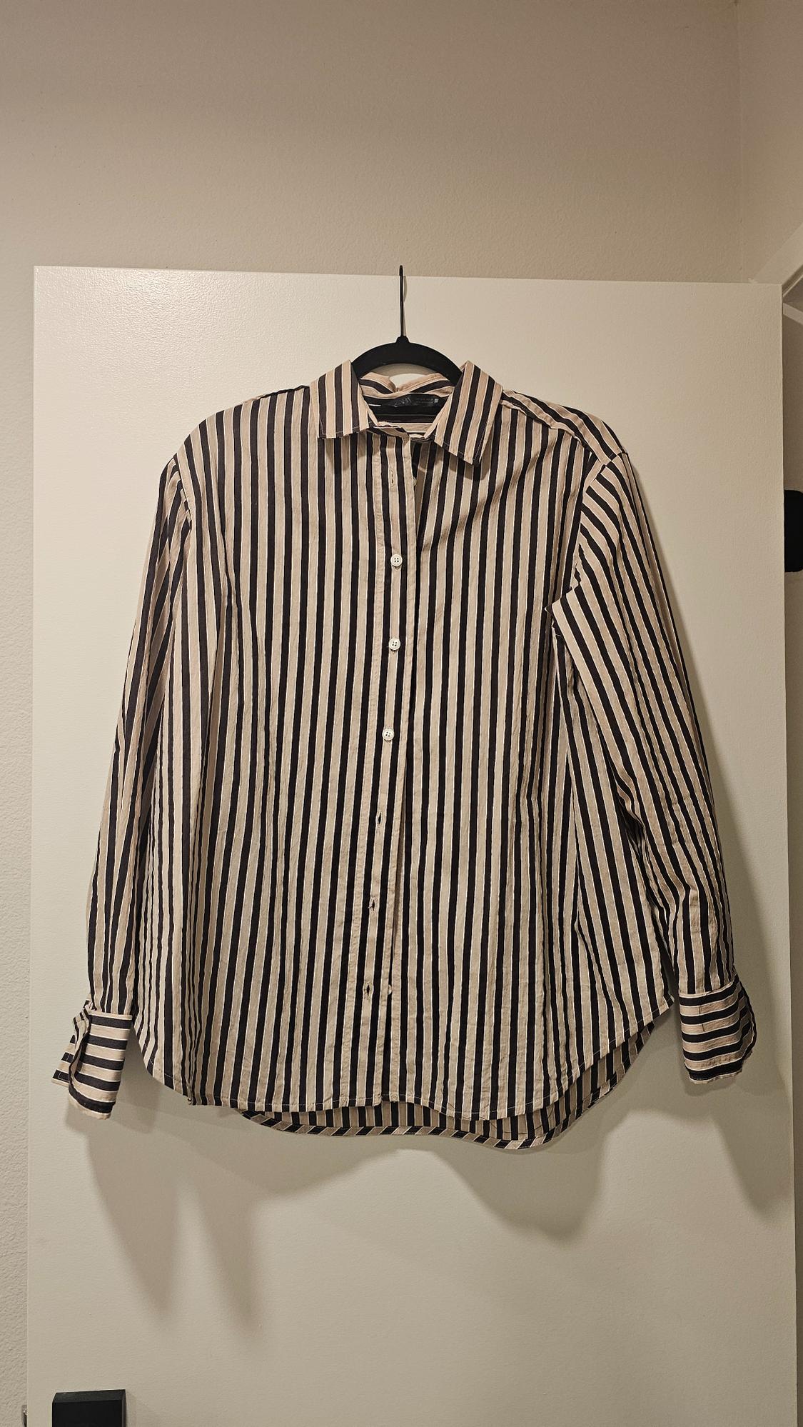 Black and beige vertical striped shirt hanging on a hanger over a white door. Long sleeves and front buttons.