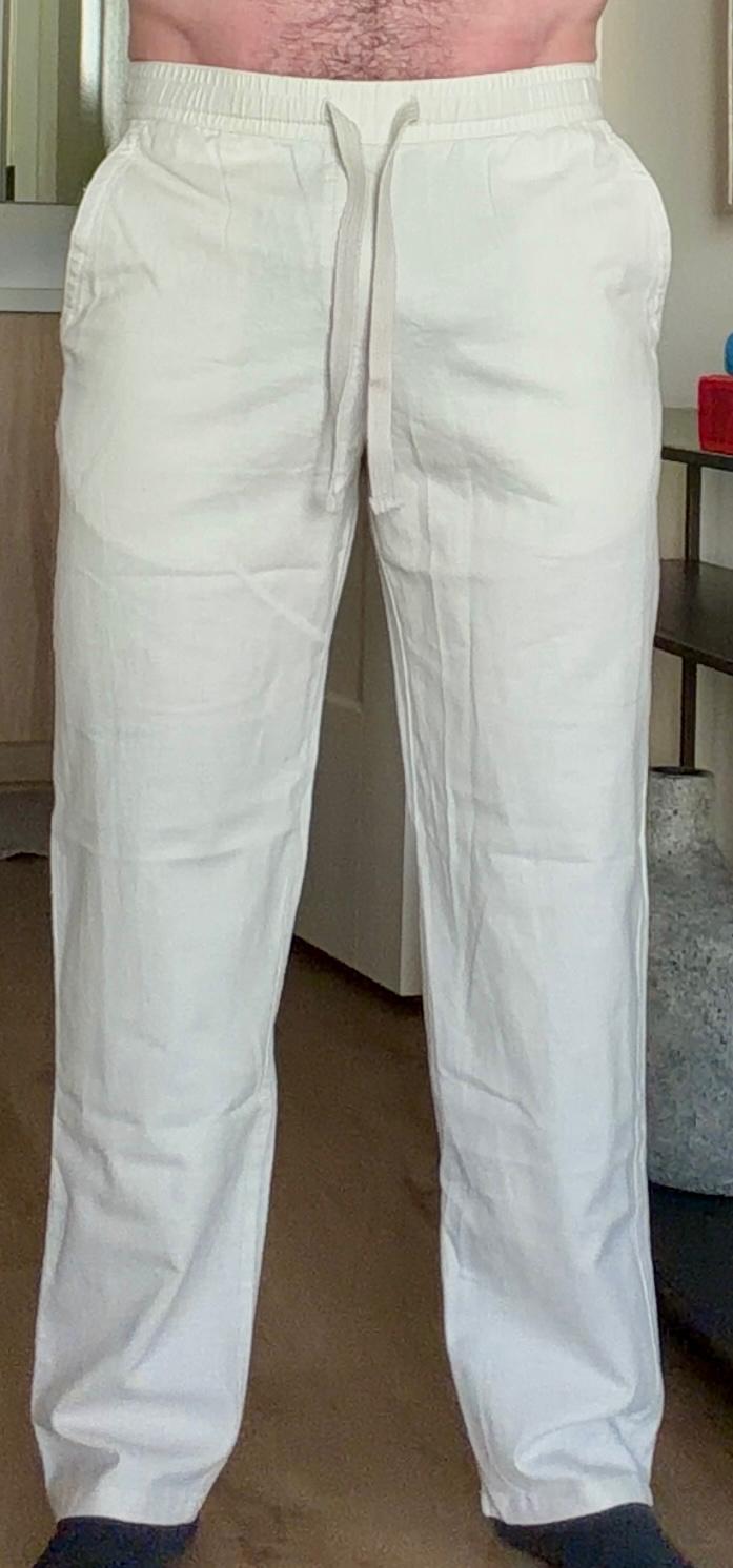 Man wearing loose white trousers with an elastic waistband and drawstring in a casual indoor setting.