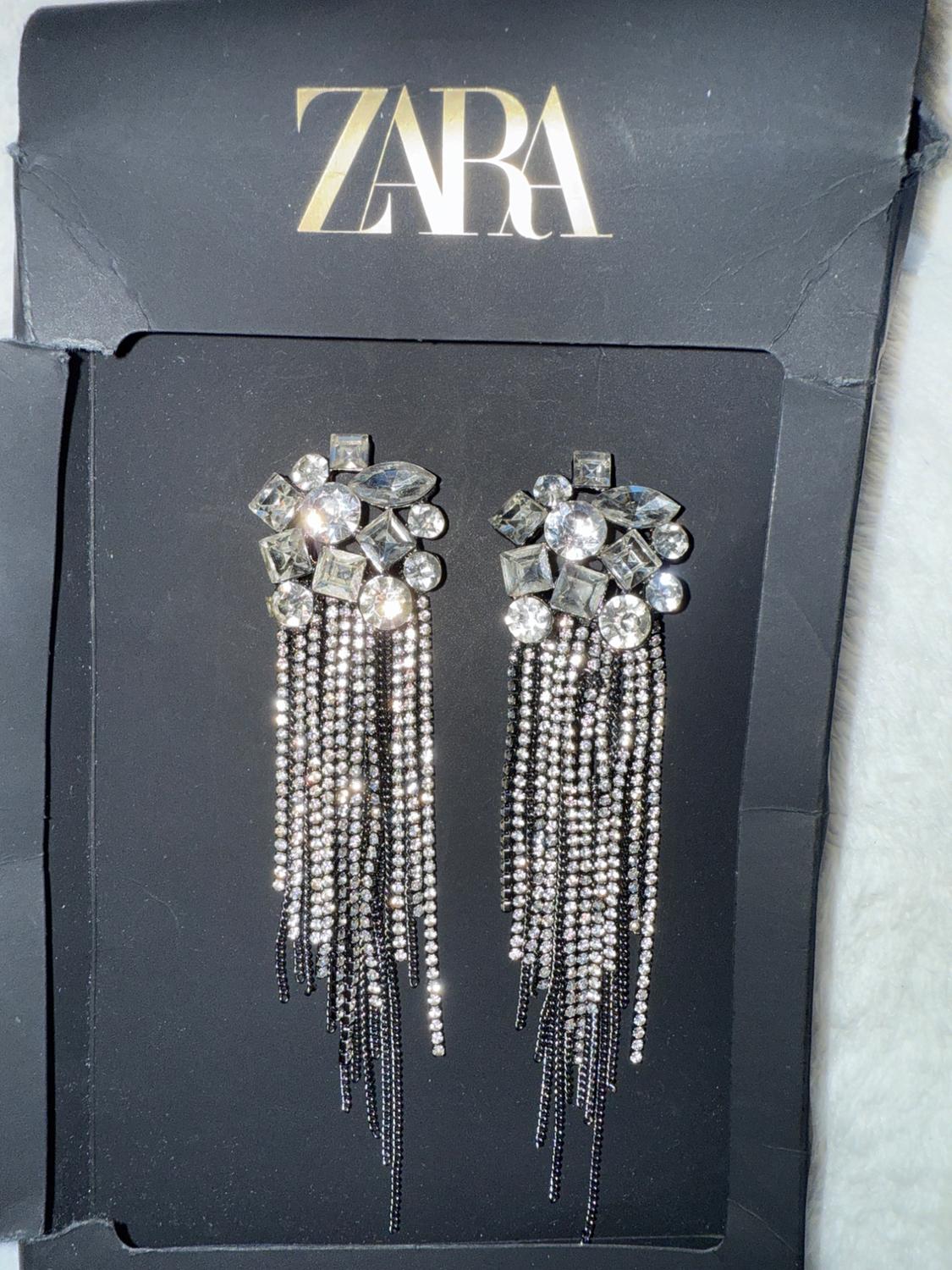 Crystal drop earrings with a geometric design on a black background. Visible text: "ZARA" at the top.