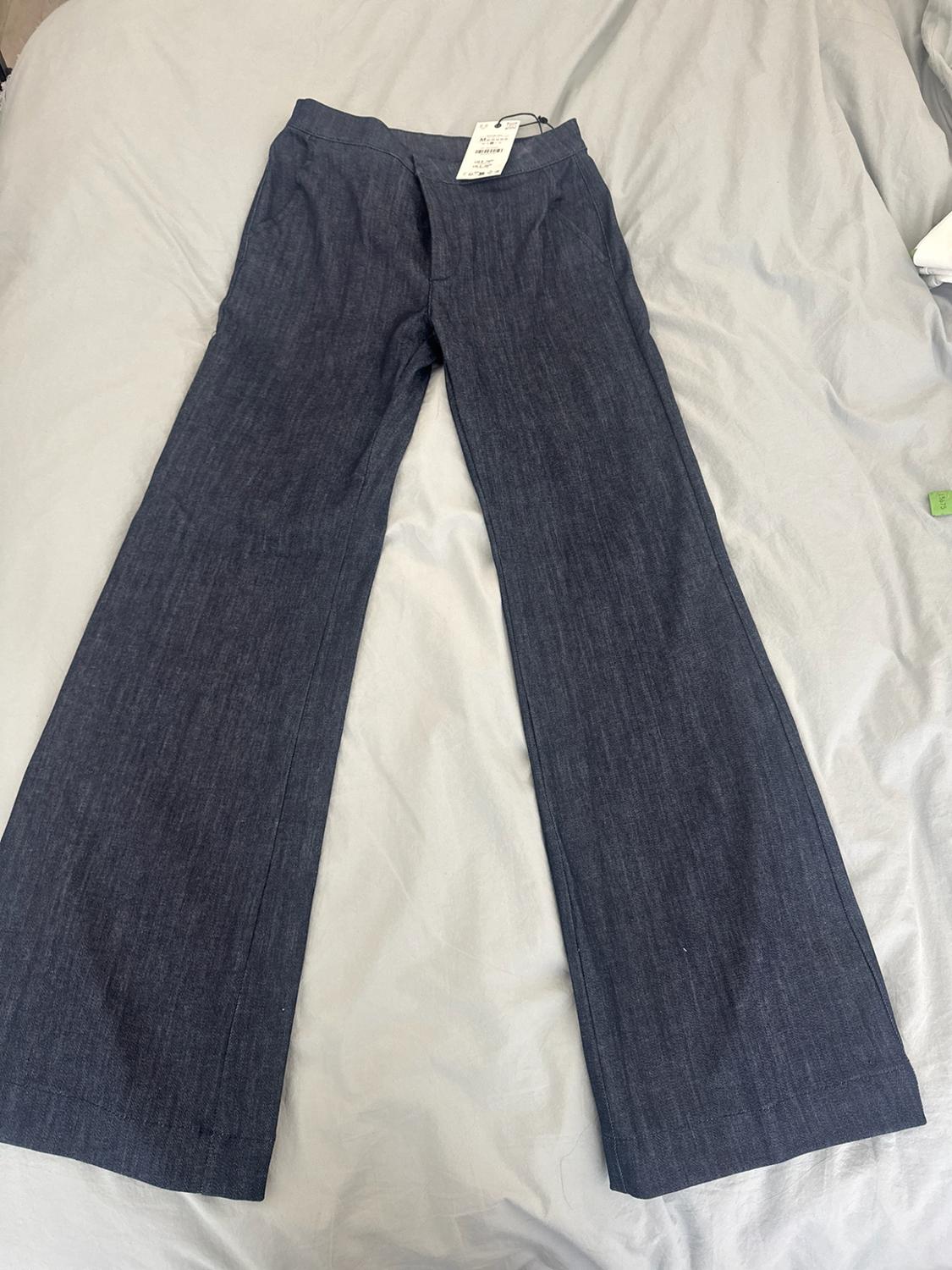 Dark blue wide-leg jeans with tags, spread out on some crumpled light-coloured sheets.