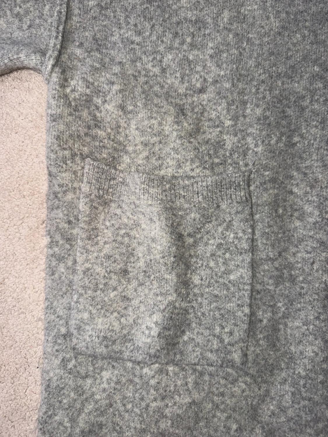 Close-up of a heather grey knitted fabric with a large square pocket, on a light background. Relaxed and cosy style.