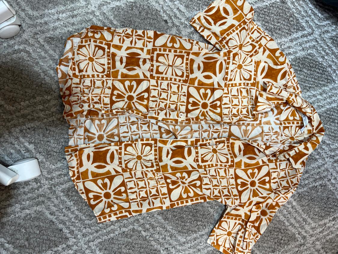 Short-sleeved shirt with geometric print in brown and white tones, on a textured grey rug.