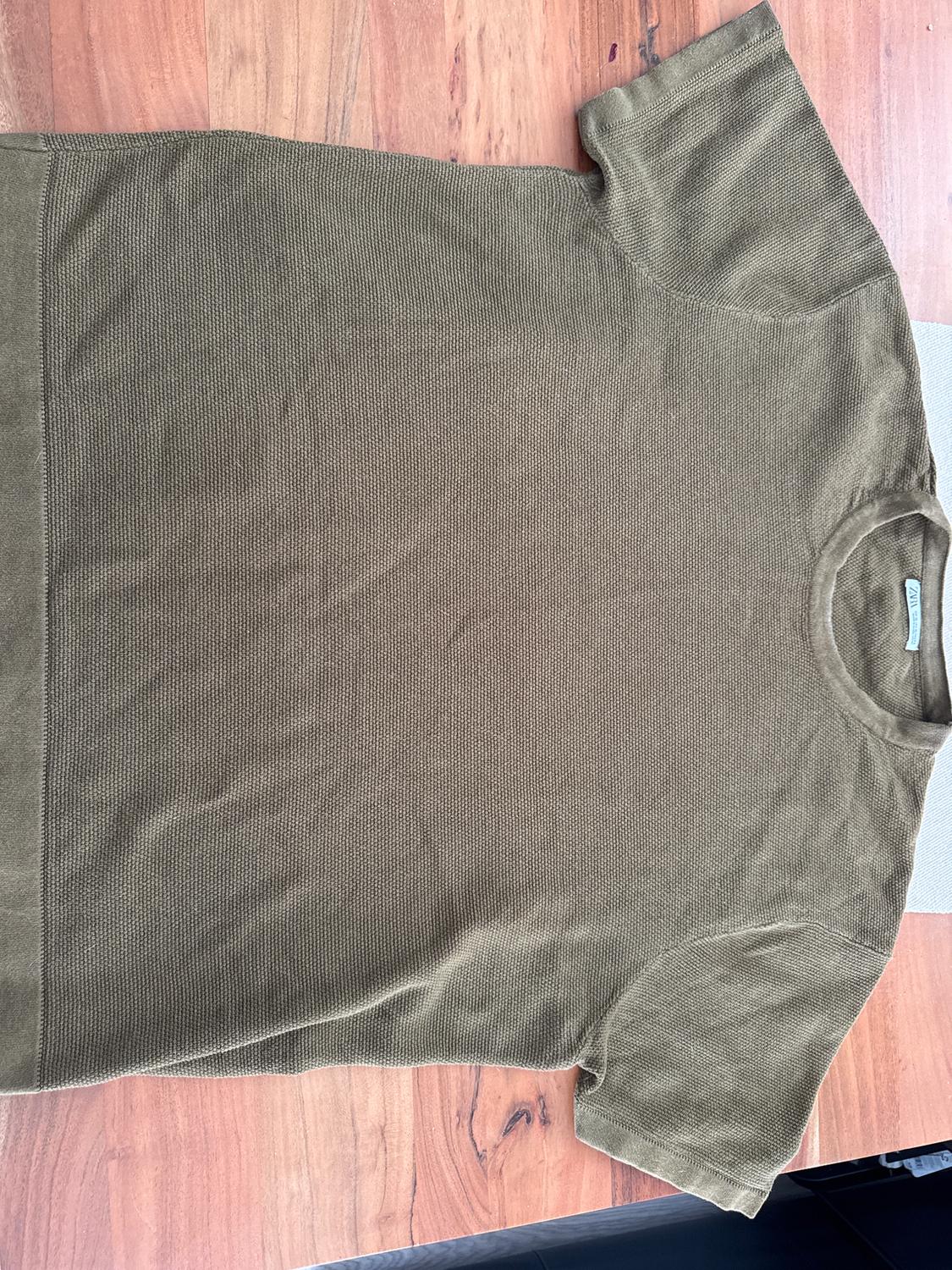 Olive green knitted t-shirt on a wooden table. Simple design with short sleeves and a round neck.