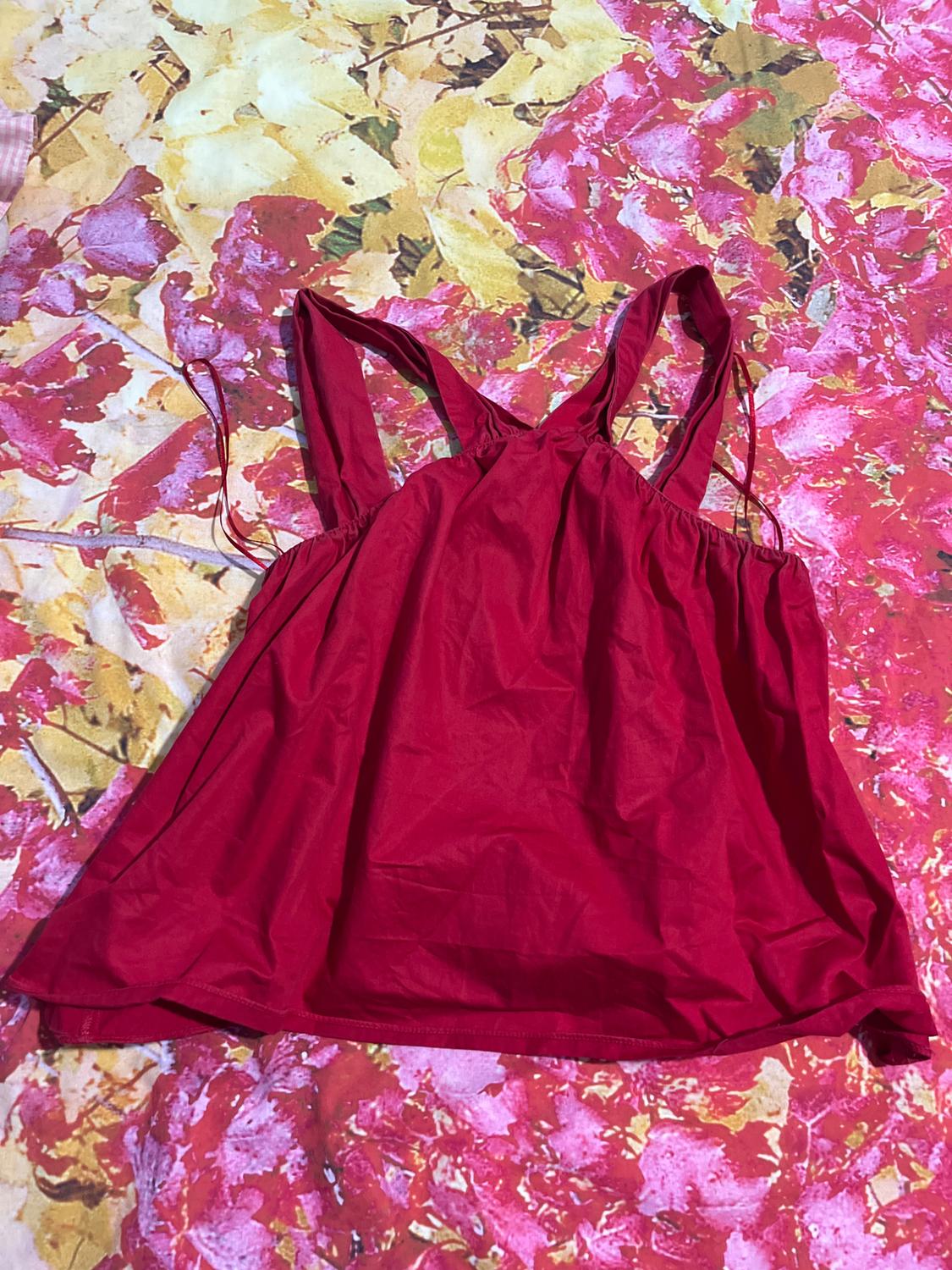 Red strappy top on a background of yellow and pink leaves. Crinkled fabric and loose design.