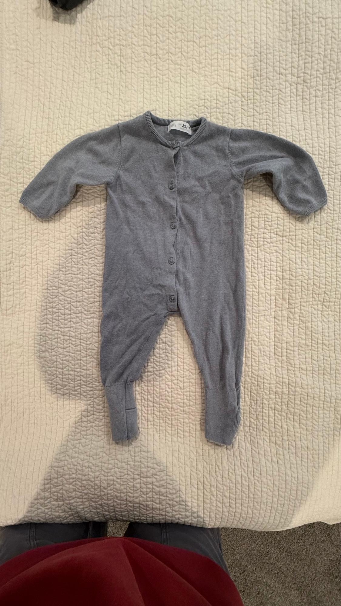 Grey babygrow with buttons down the front, on a textured white quilt. Lower half of a person visible.